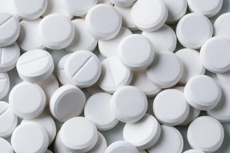Scattered white round pharmaceutical tablets on a plain surface