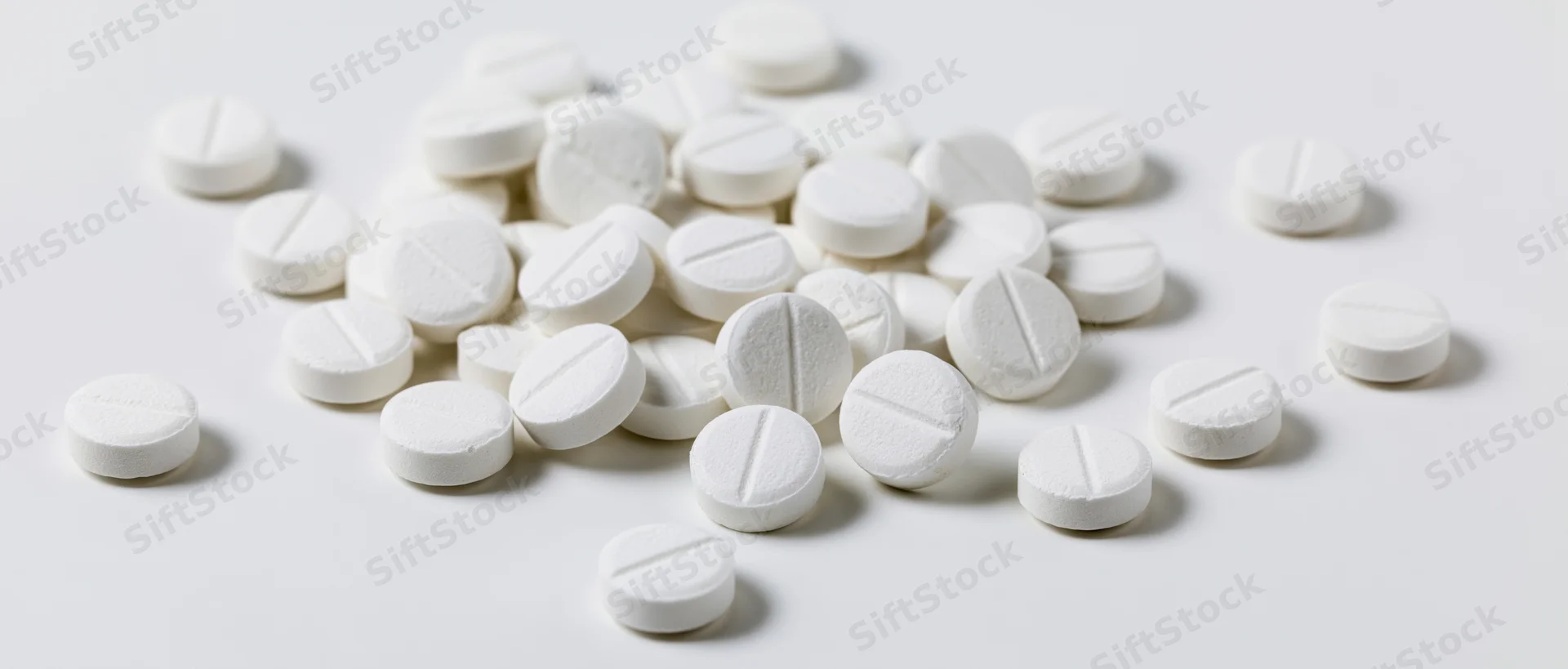 Scattered white scored tablets on a plain white surface