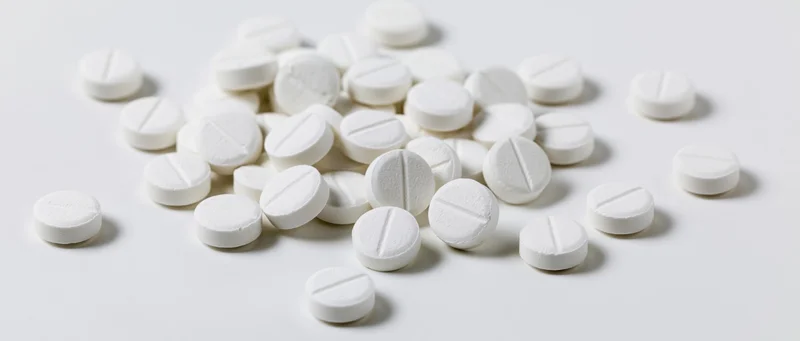 Scattered white scored tablets on a plain white surface