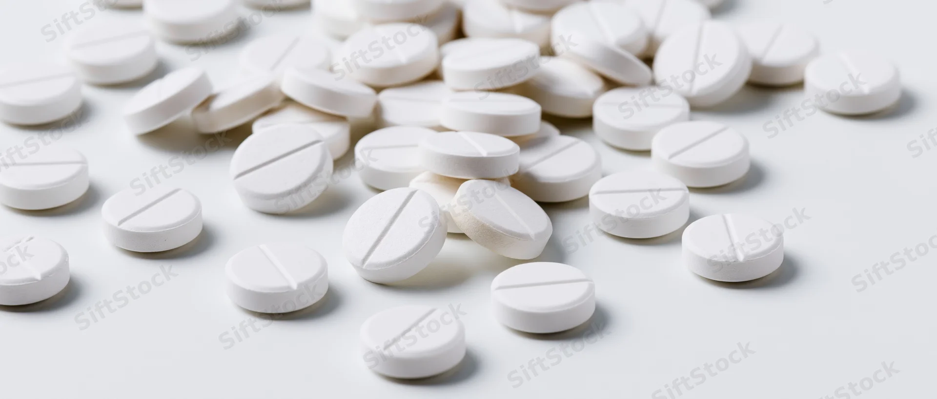 Scattered white scored tablets on a plain white surface