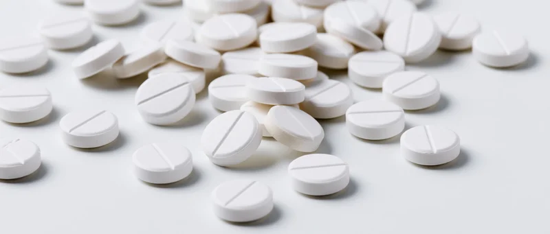 Scattered white scored tablets on a plain white surface