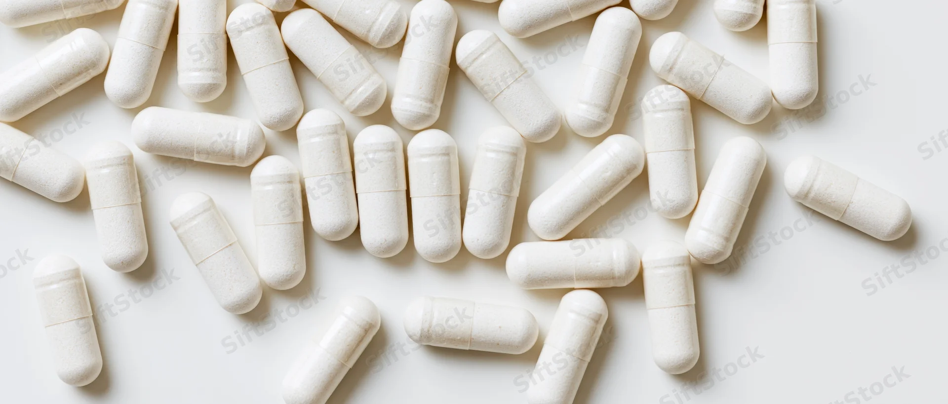 White supplement capsules scattered on a plain white surface