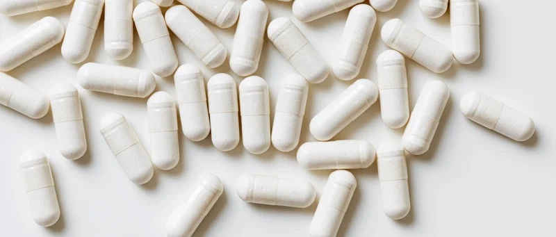 White supplement capsules scattered on a plain white surface