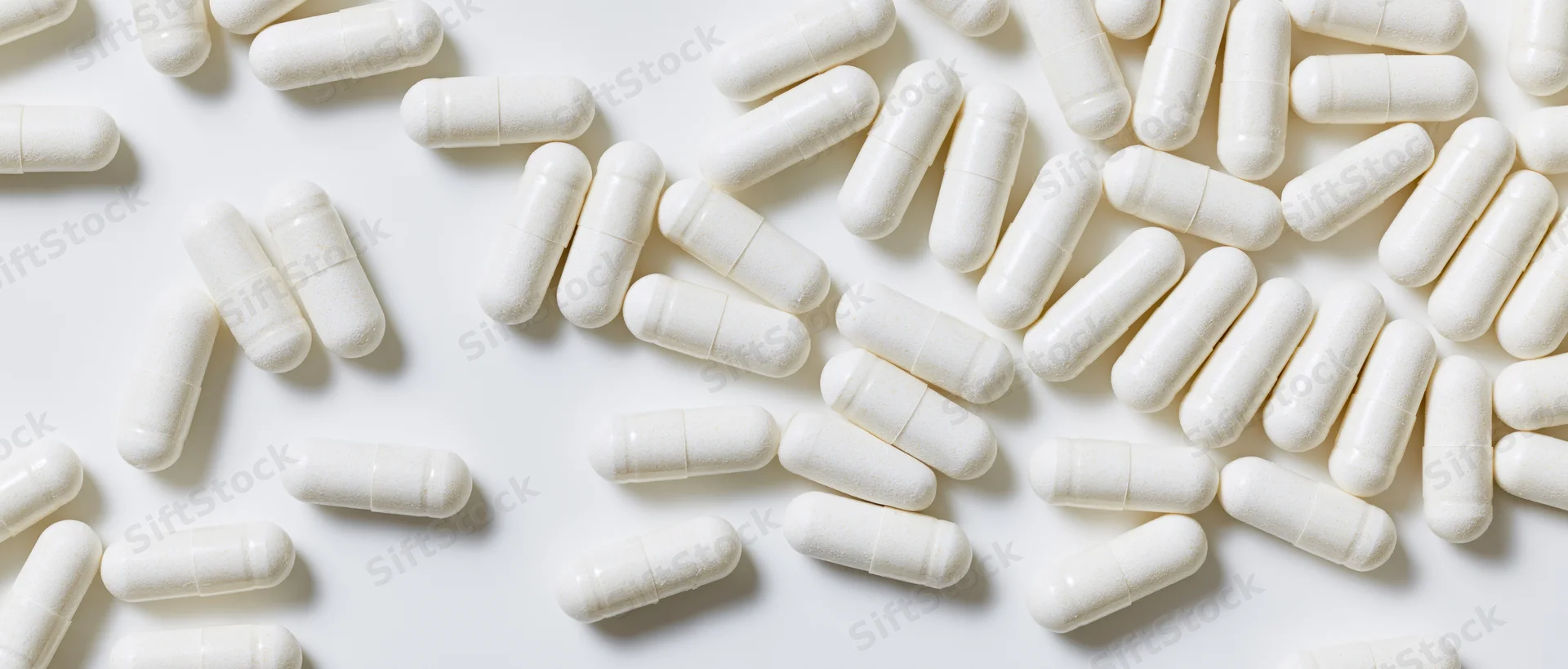 White oblong supplement capsules scattered across a plain white surface