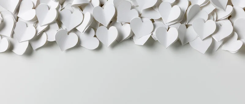 White paper hearts scattered along the top edge of a plain surface, leaving copyspace below