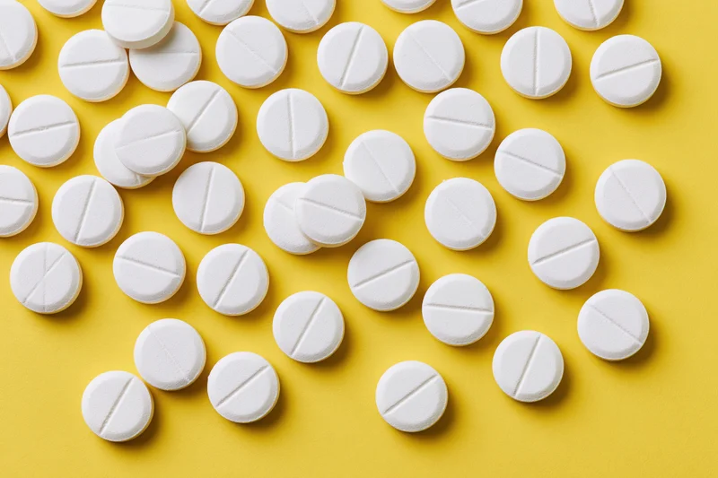 White round pharmaceutical tablets scattered across a yellow background