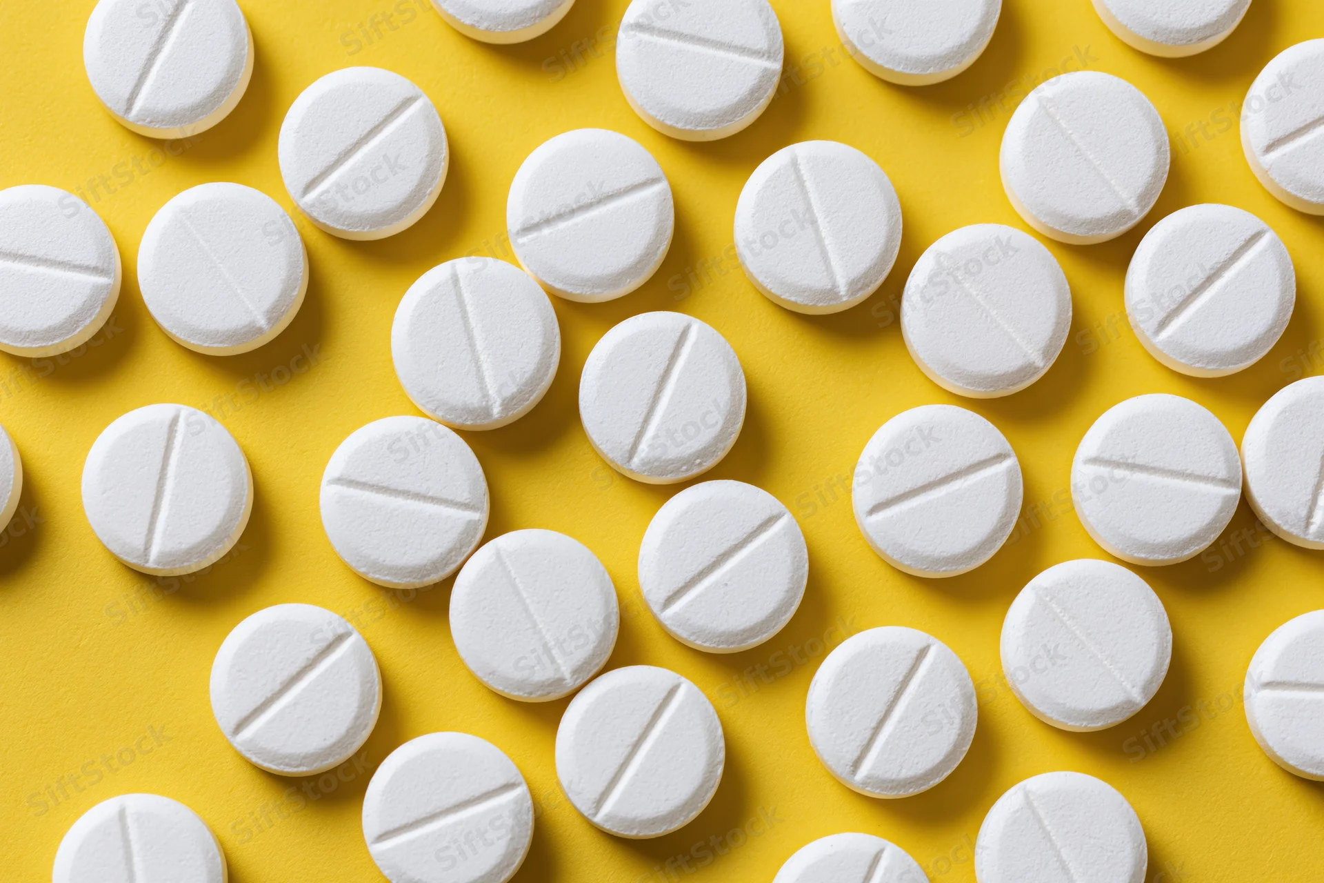 White round pharmaceutical tablets scattered on yellow background