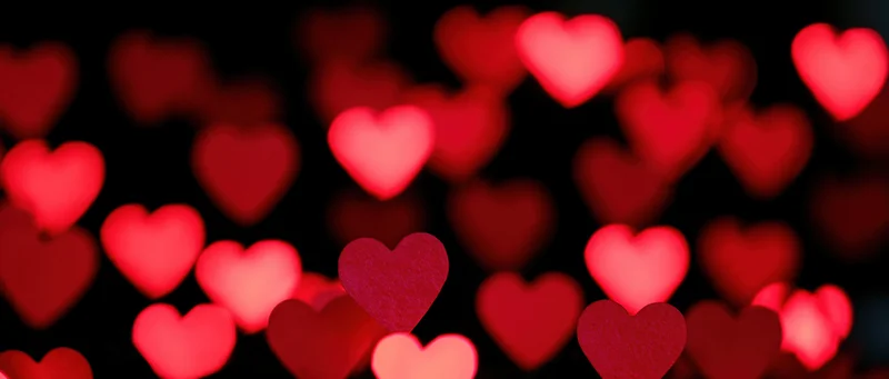 Soft red heart-shaped bokeh lights glowing against a dark background
