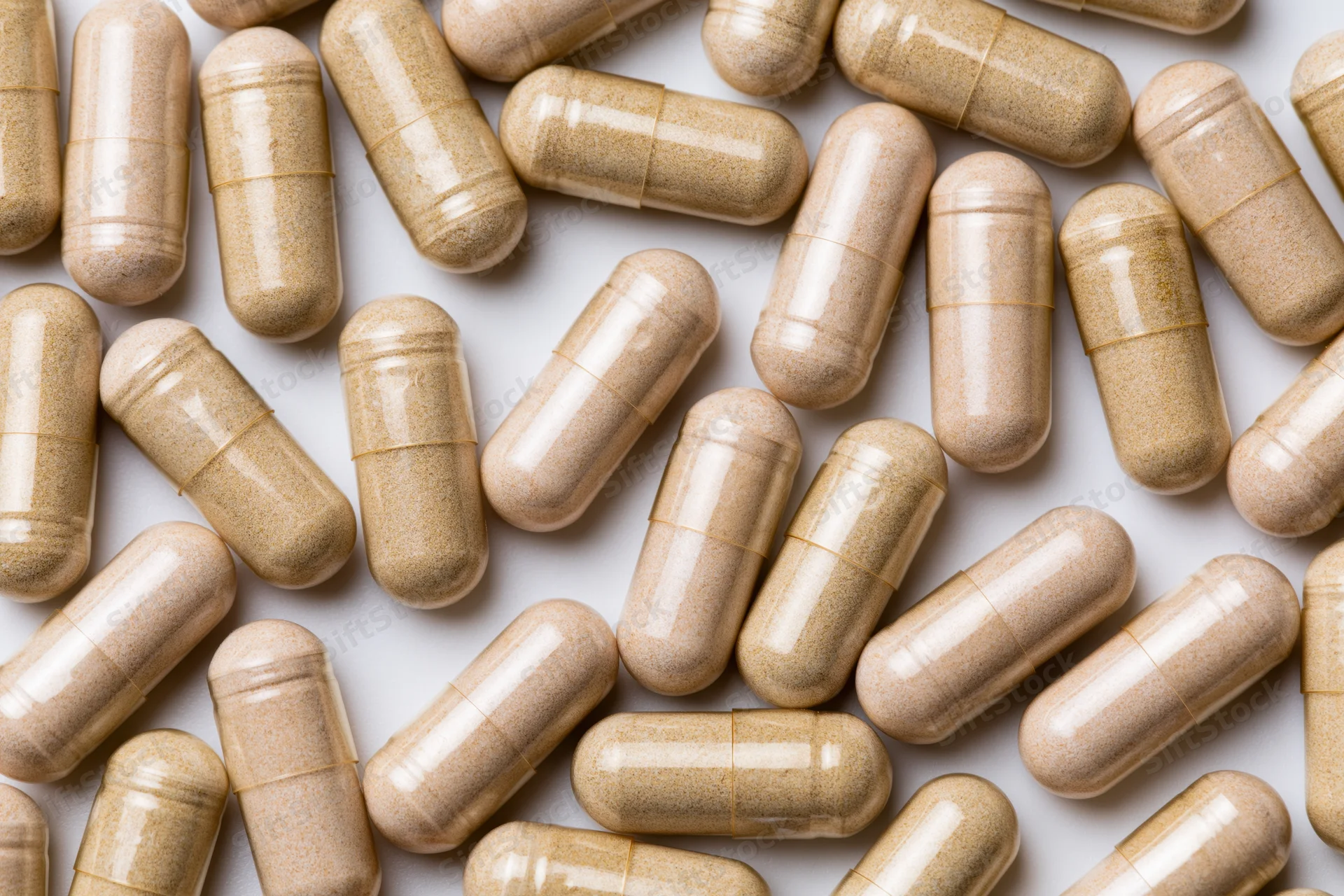 Tan herbal supplement capsules scattered randomly on white surface