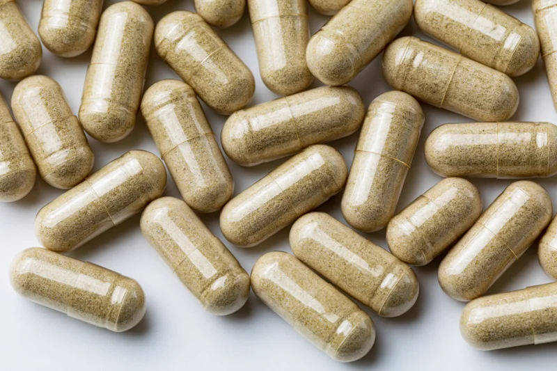 Tan herbal supplement capsules scattered randomly on white surface