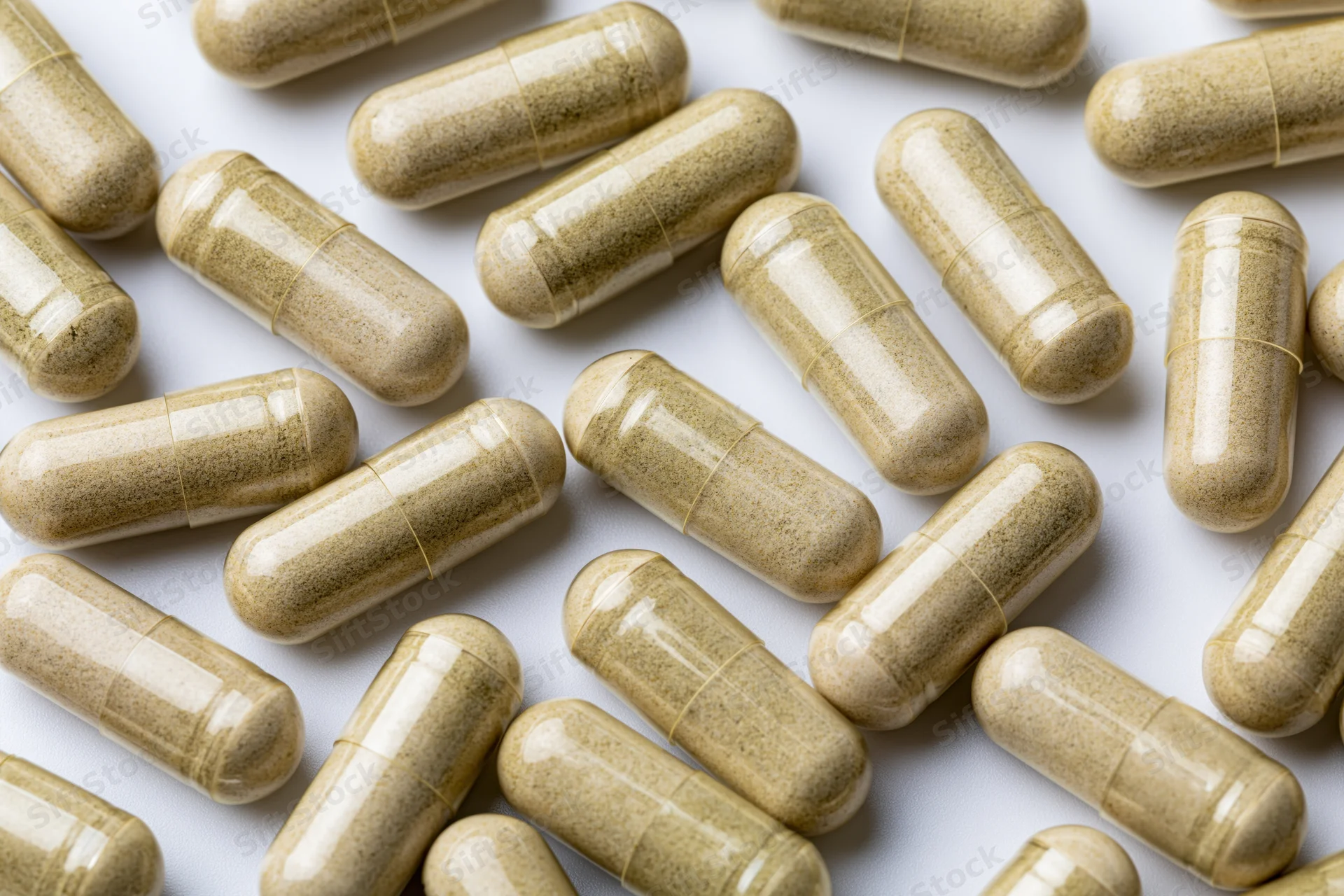 Tan herbal supplement capsules scattered randomly on white surface