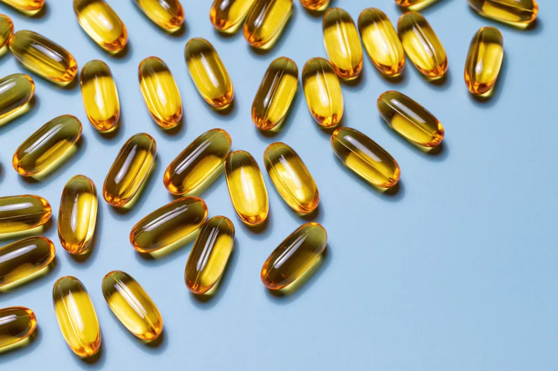 Translucent amber gel capsules scattered loosely on a blue surface