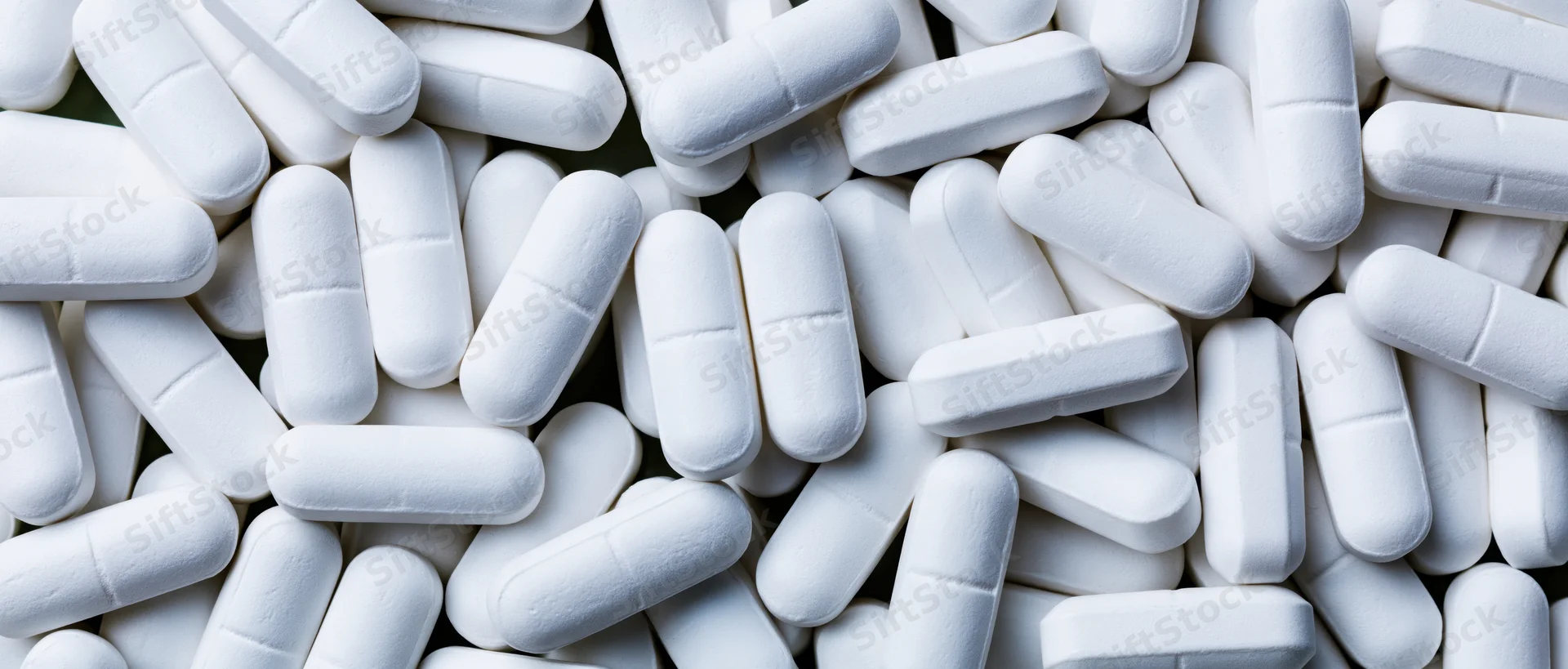 White oblong pharmaceutical tablets scattered in a pile