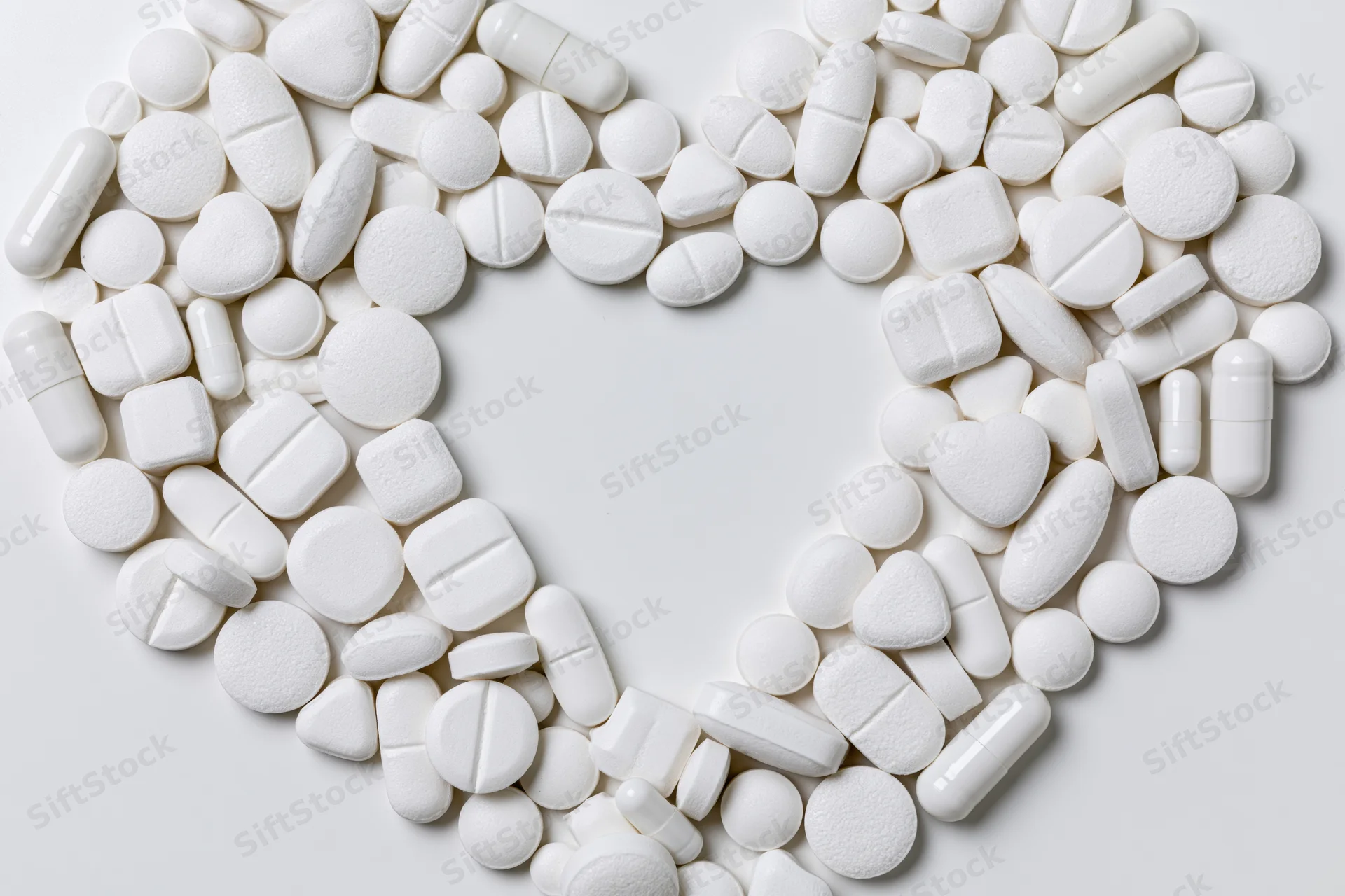 White pharmaceutical tablets and capsules arranged in heart shape on plain surface