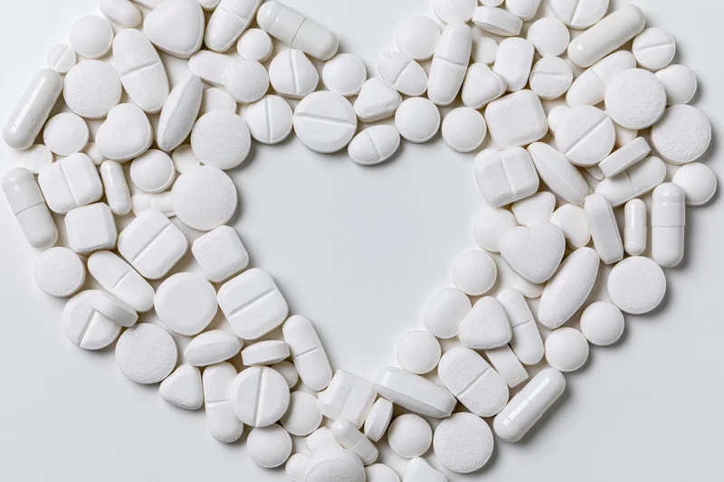 White pharmaceutical tablets and capsules arranged in heart shape on plain surface
