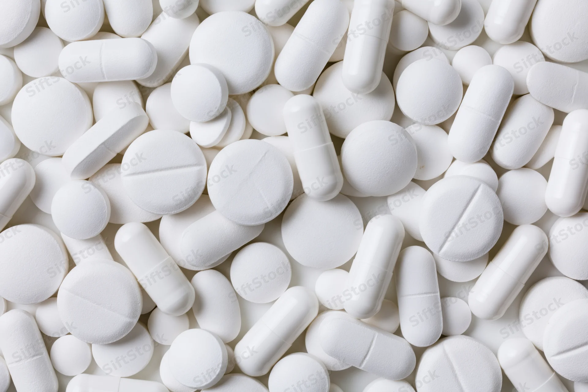 White pharmaceutical tablets and capsules scattered in close-up view