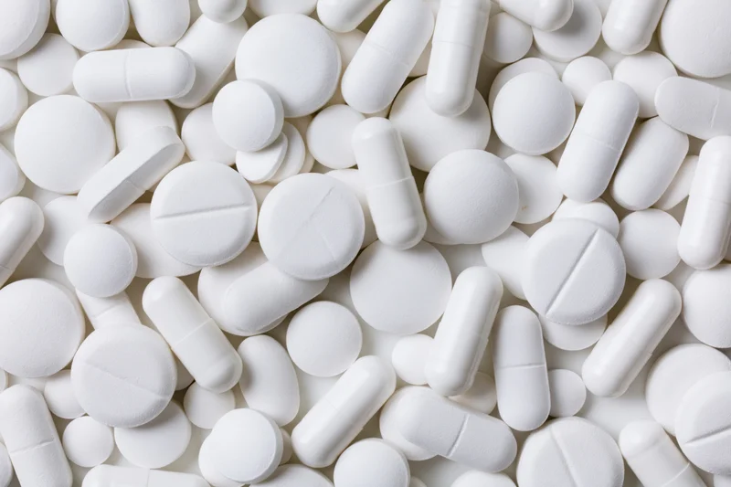 White pharmaceutical tablets and capsules scattered in close-up view