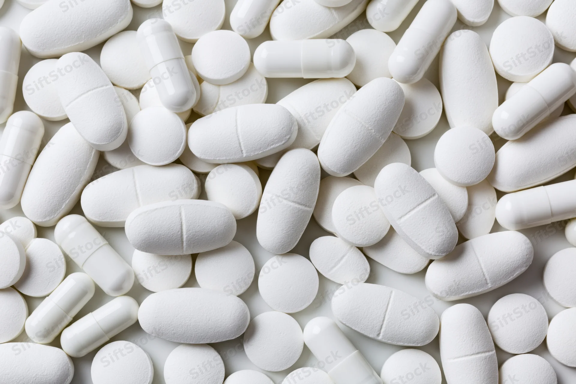 White pharmaceutical tablets and capsules scattered on a plain surface