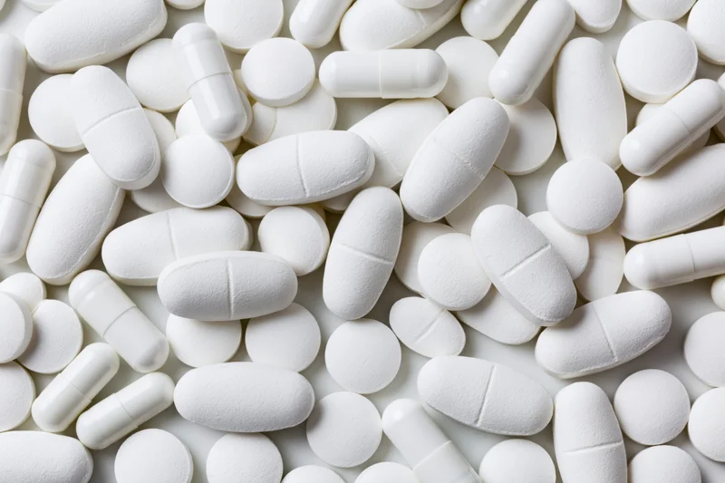 White pharmaceutical tablets and capsules scattered on a plain surface