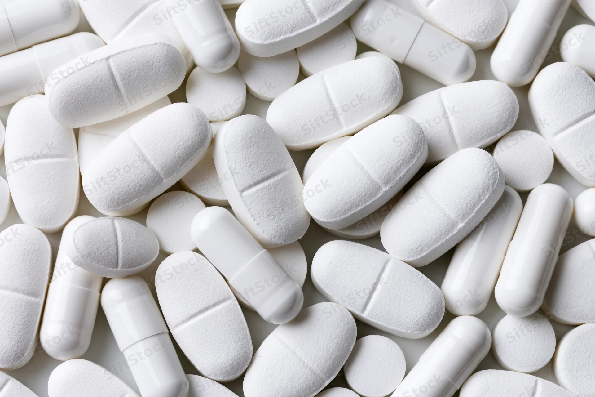 White pharmaceutical tablets and capsules scattered in close-up view