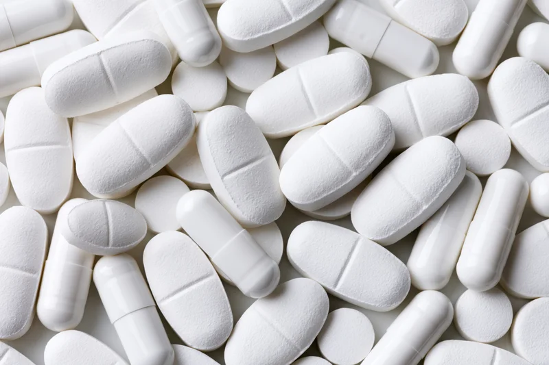 White pharmaceutical tablets and capsules scattered in close-up view