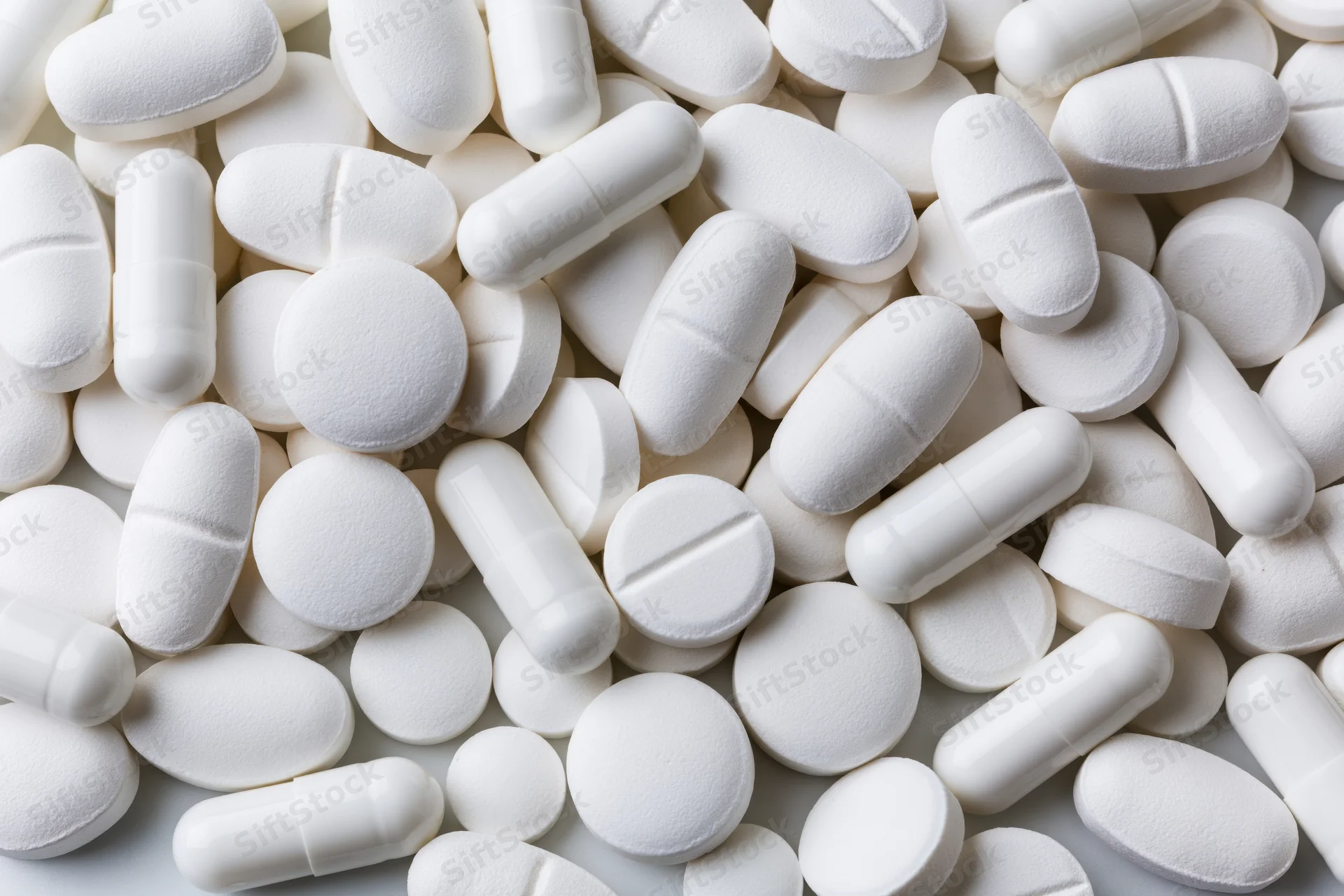White pharmaceutical tablets and capsules scattered in close-up view