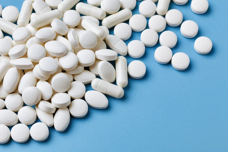 White pharmaceutical tablets and capsules scattered on blue surface