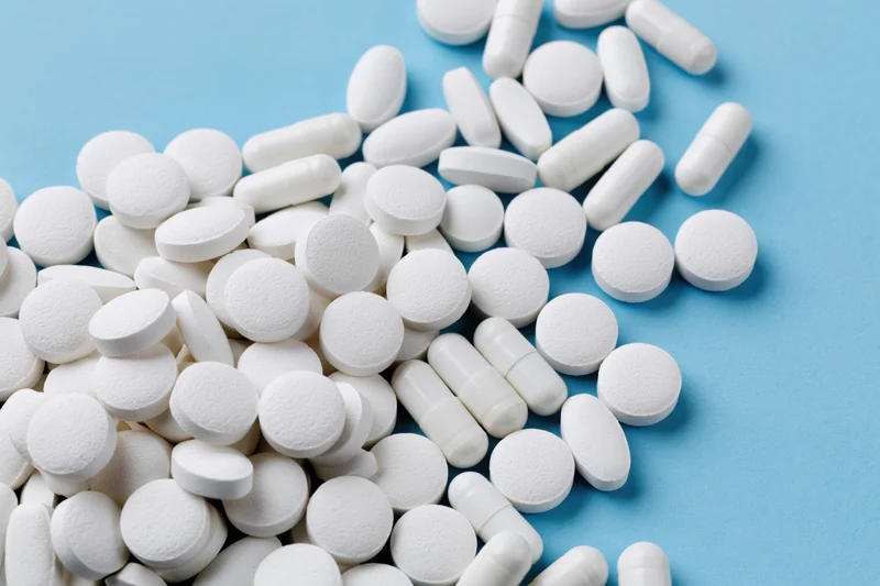 White pharmaceutical tablets and capsules scattered on a blue surface