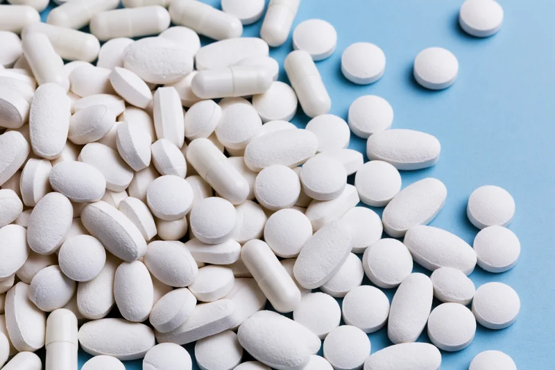 White pharmaceutical tablets and capsules scattered on a blue surface