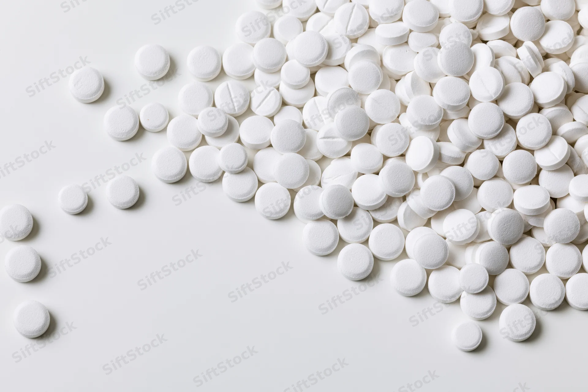 White round pharmaceutical tablets scattered across a plain white surface with copyspace on the left