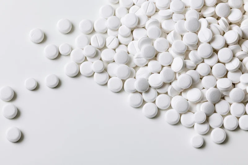 White round pharmaceutical tablets scattered across a plain white surface with copyspace on the left