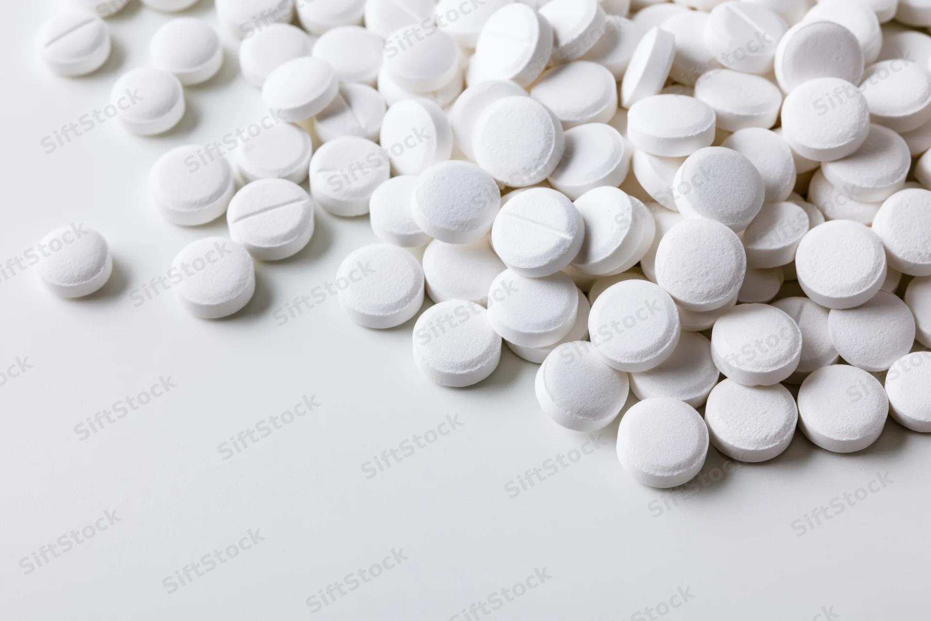 White round pharmaceutical tablets scattered on a smooth white surface with copyspace