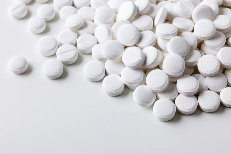 White round pharmaceutical tablets scattered on a smooth white surface with copyspace