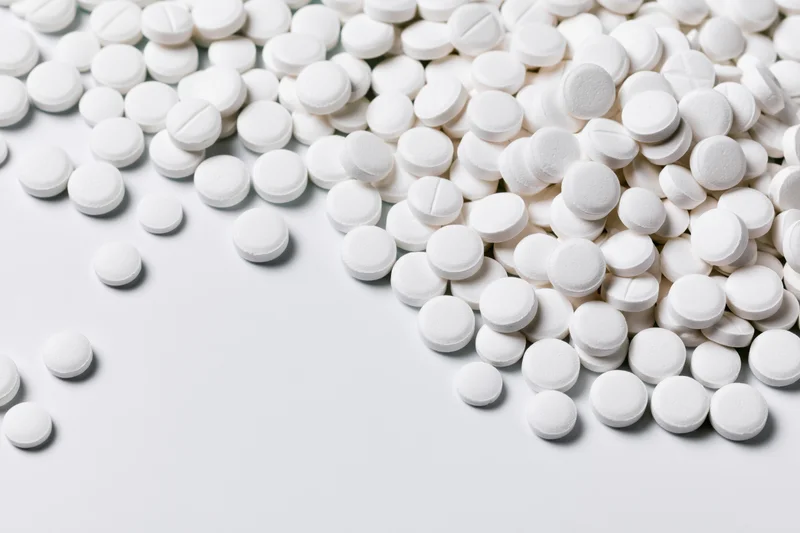 White round pharmaceutical tablets scattered on a plain white surface with copyspace