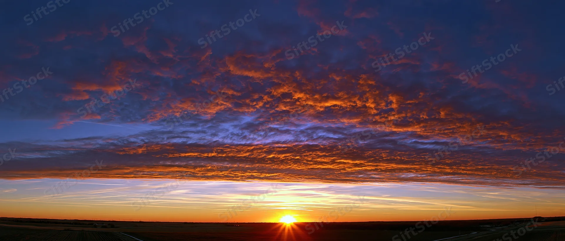 Dramatic sunset sky with fiery clouds above flat rural horizon