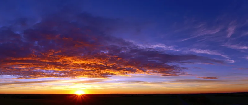 Dramatic sunset sky with fiery clouds and golden sun low on the horizon