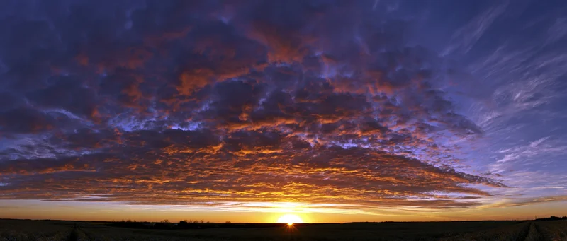 Dramatic sunset sky with vibrant orange and purple clouds over a flat rural field at dusk