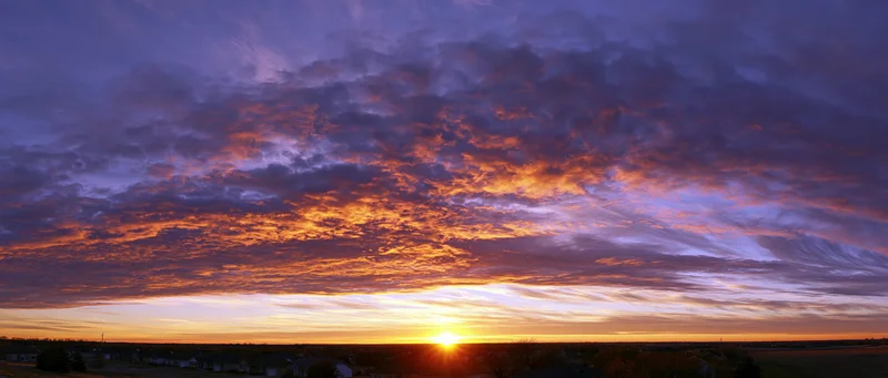 Dramatic sunset sky with fiery orange and purple clouds over rural landscape at horizon