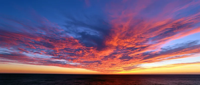 Dramatic sunset sky over the ocean with vibrant clouds and horizon line