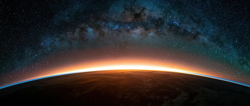 Earth's curved horizon from low orbit during golden sunrise with milky way above