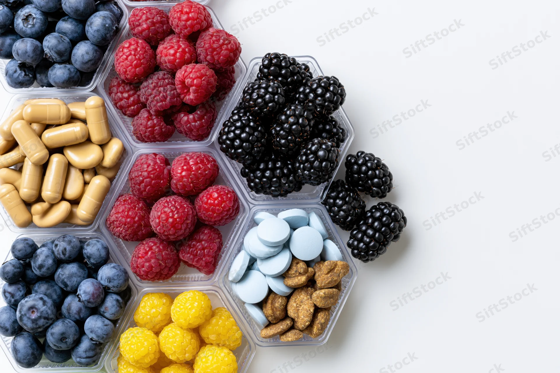 Hexagonal compartments filled with berries and dietary supplements arranged on white surface