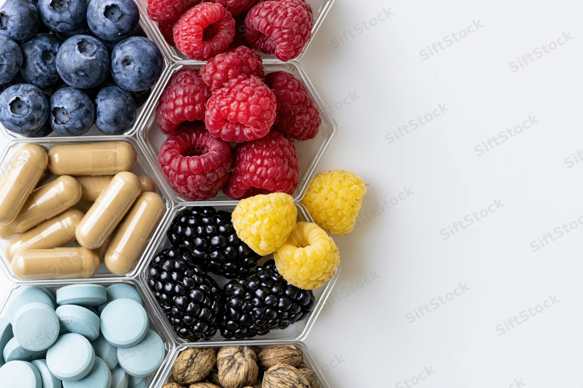 Hexagonal compartments holding berries, supplements, and nuts arranged on white surface with copyspace