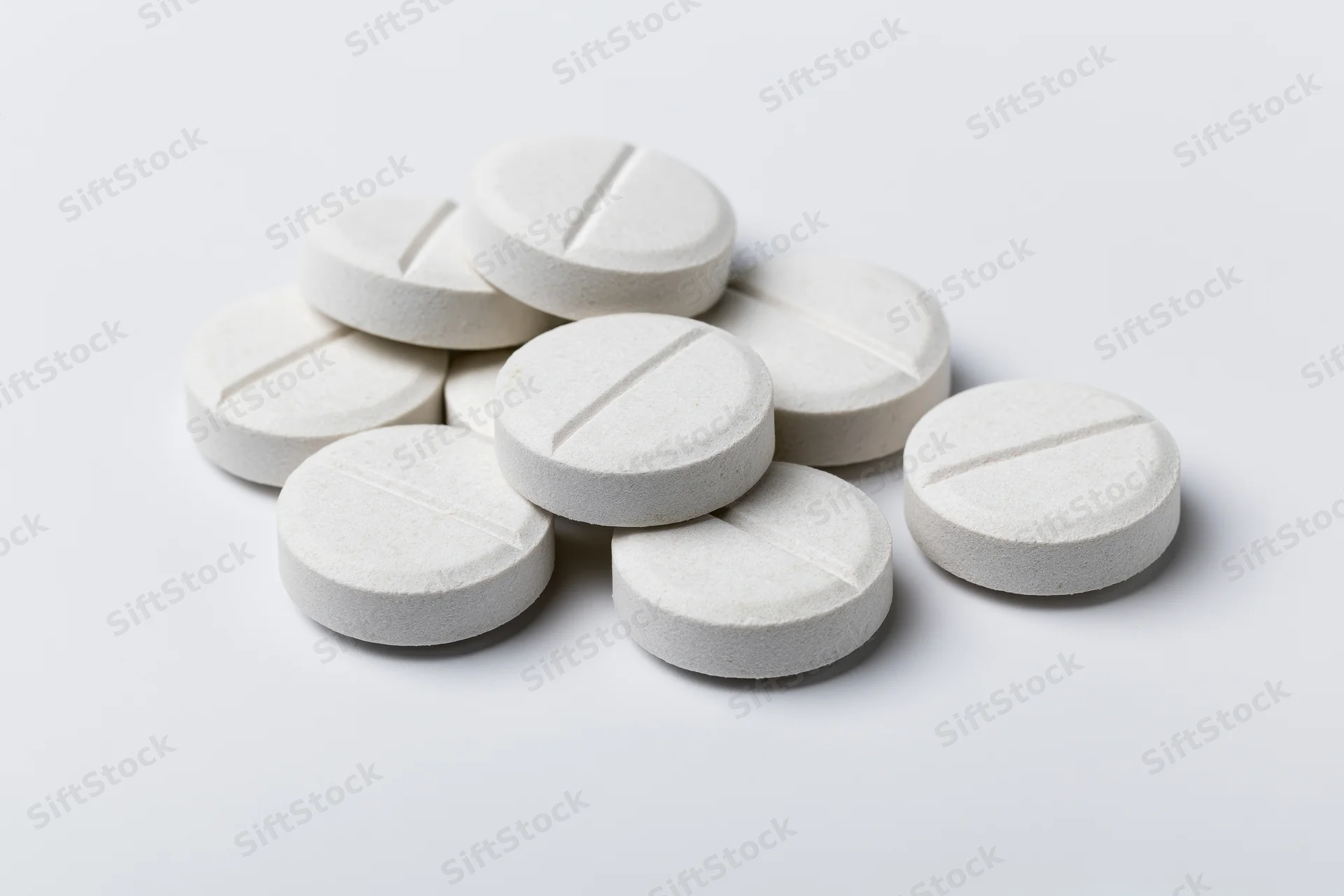 White scored tablets scattered loosely on a plain white surface