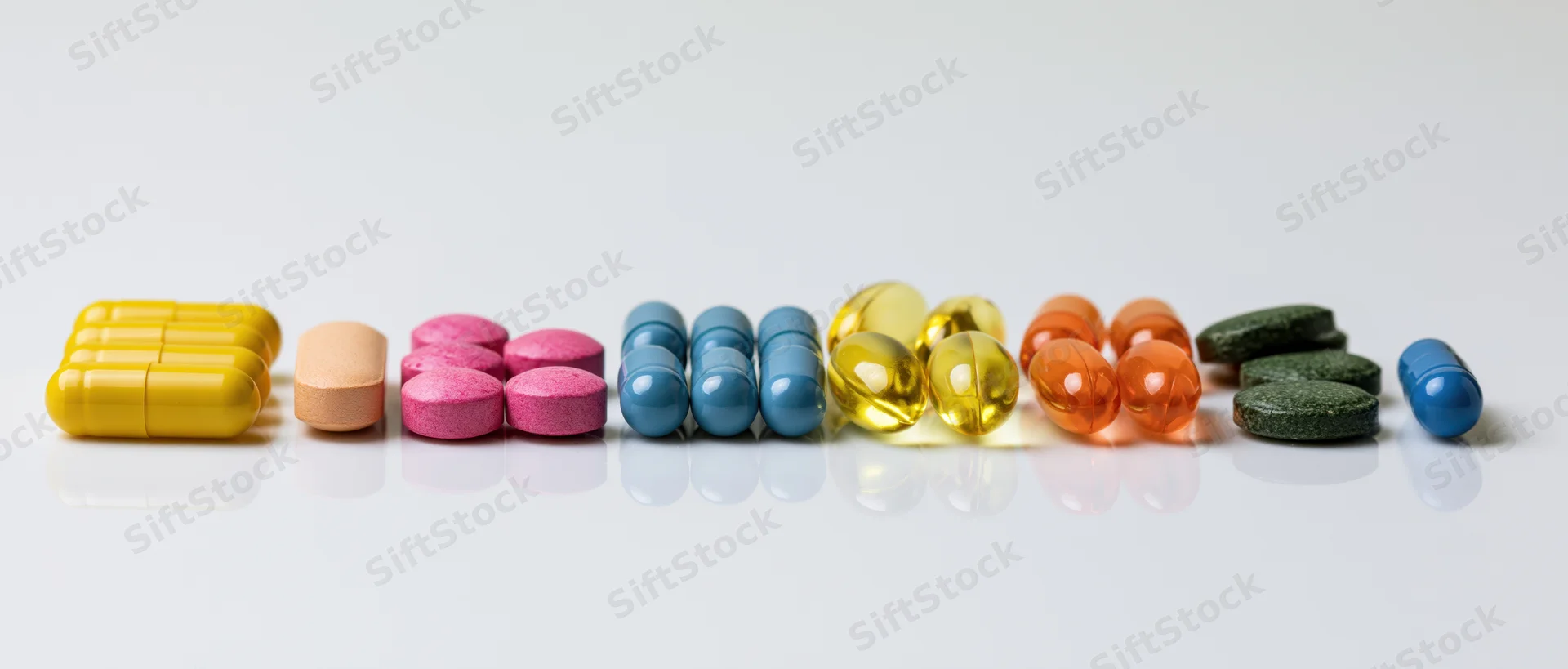 Assorted pills and capsules arranged in groups on a reflective white surface