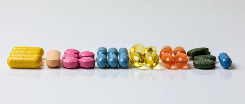 Assorted pills and capsules arranged in groups on a reflective white surface
