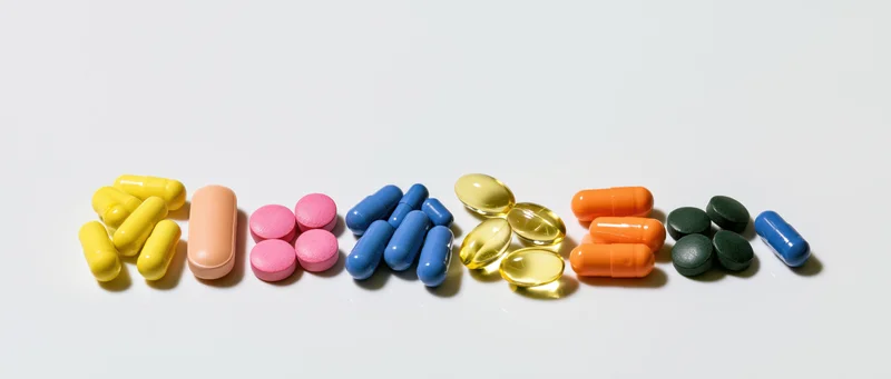 Assorted pills and capsules arranged in small groups on a white surface