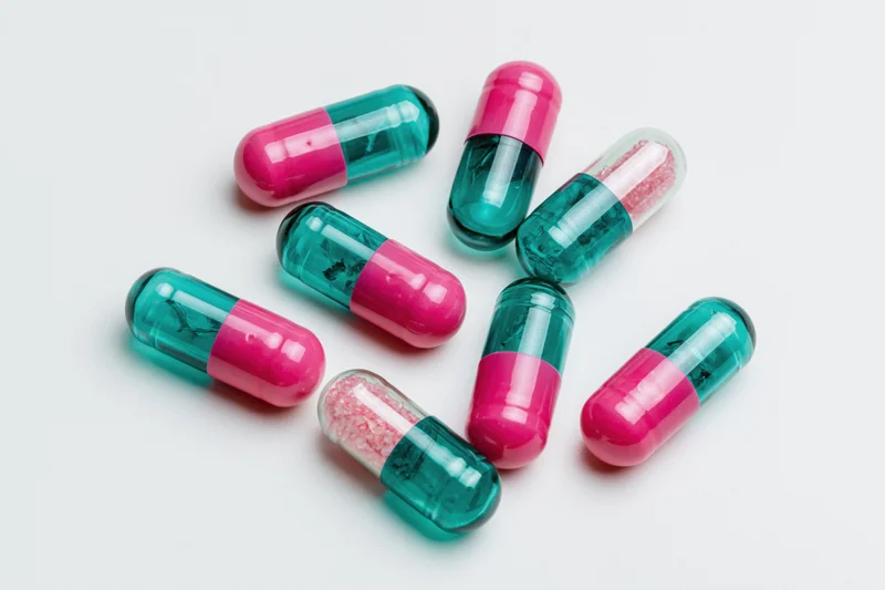 Scattered two-tone pharmaceutical capsules on white surface