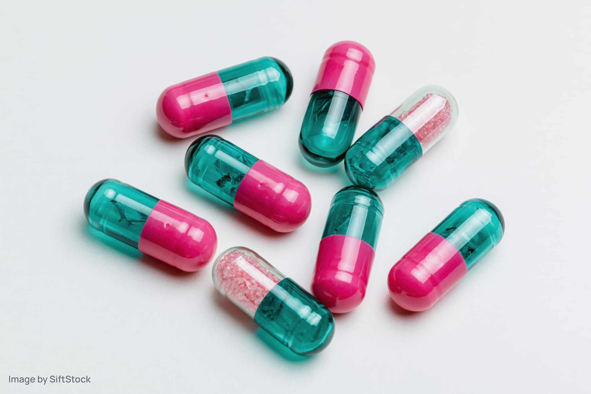Scattered two-tone pharmaceutical capsules on white surface