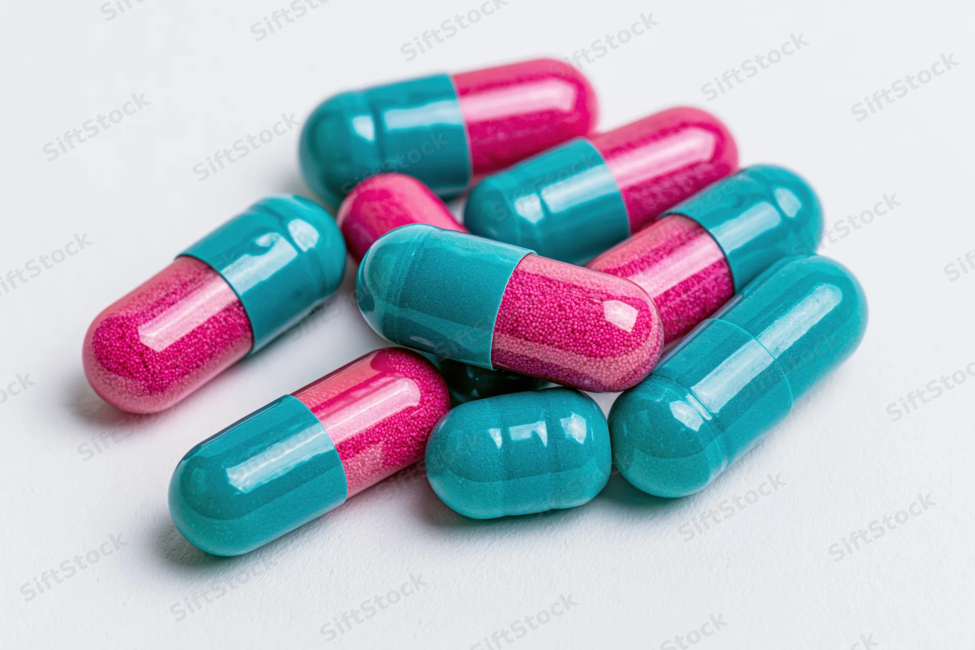 Scattered two-tone pharmaceutical capsules on white surface
