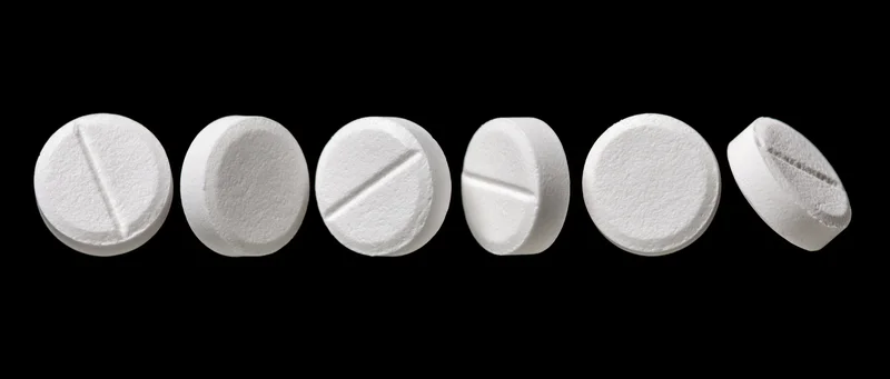 Six white round pharmaceutical tablets arranged in a row on black background